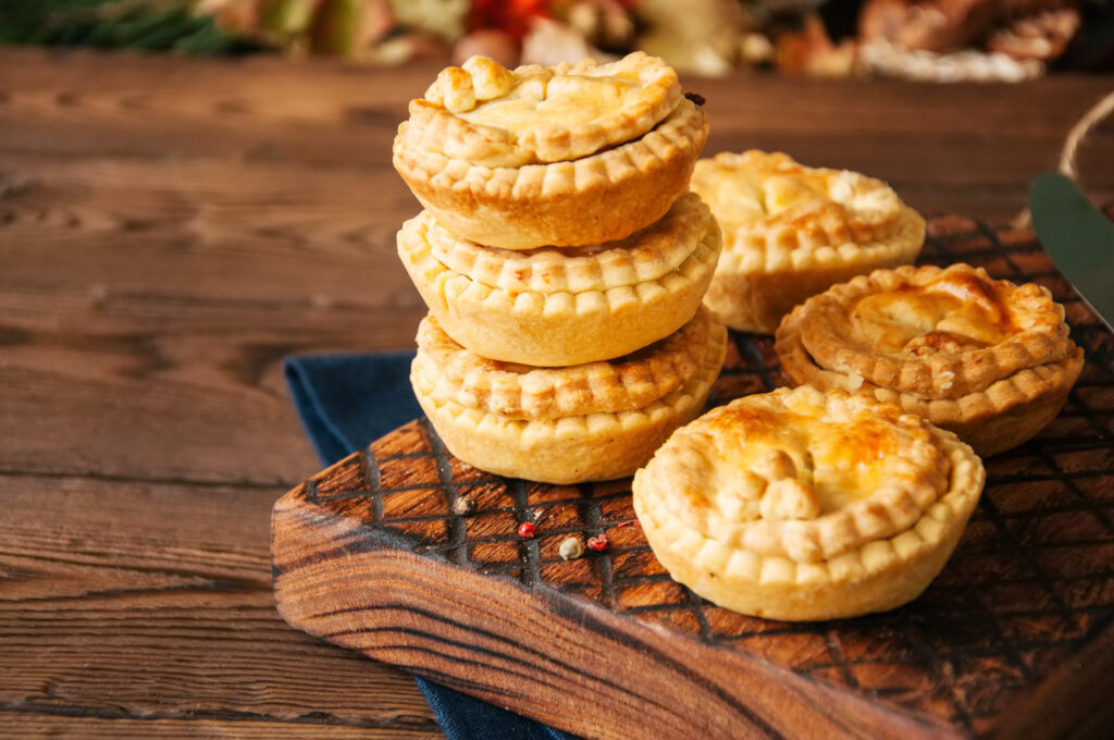 Mini meat pies from flaky dough on a wooden board over wooden background.